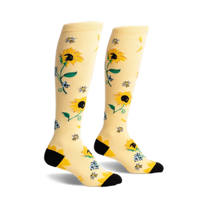 Pair of knee-high socks in pale yellow with a sunflower, bee, and floral design. Black heel and toe.