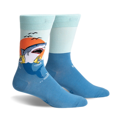 A pair of crew socks with a graphic of a shark catching a life preserver at sunset. The socks are teal and light blue.