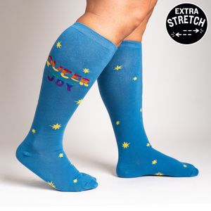 Lifestyle shot: Person wearing blue knee-high socks with 'Queer Joy' and stars. Shows the fit and style.