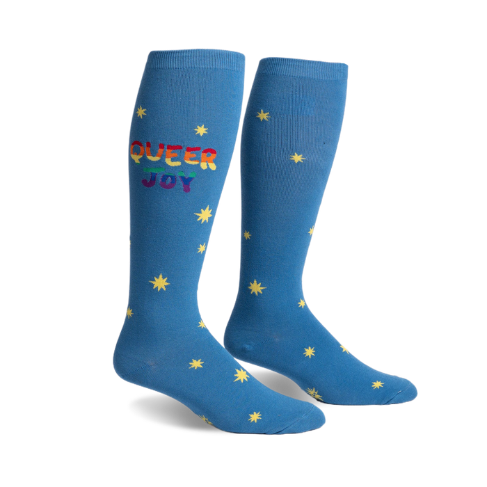 Pair of blue knee-high socks.  Rainbow 'Queer Joy' text and yellow star pattern.