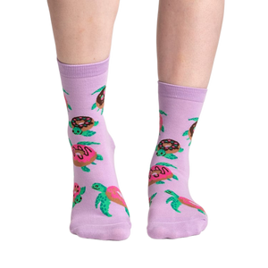 Lifestyle shot of model wearing a pair of lavender crew socks with turtles and donuts.