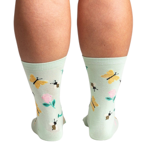 A pair of light green socks with a pattern of pink roses, yellow butterflies, and black bees.