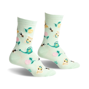 Pair of mint green crew socks with a whimsical garden design. Features bees, flowers, seed packets, and watering cans.