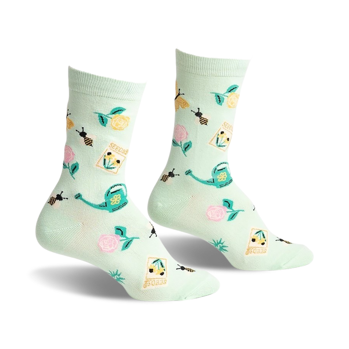 Pair of mint green crew socks with a whimsical garden design. Features bees, flowers, seed packets, and watering cans.
