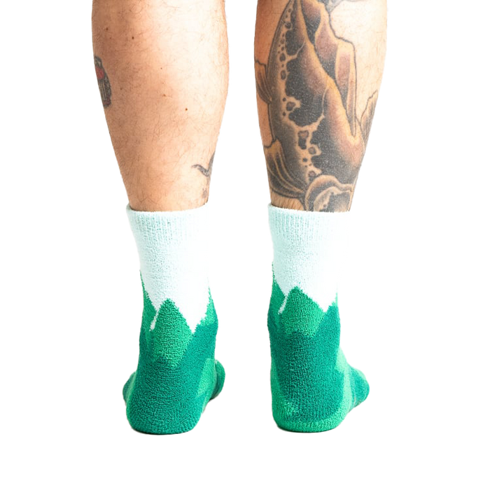 Back view of a person's legs wearing the teal and light blue mountain slipper socks, showcasing the non-slip soles.