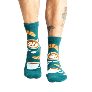 Lifestyle shot of model wearing teal blue coffee and croissant slipper socks.