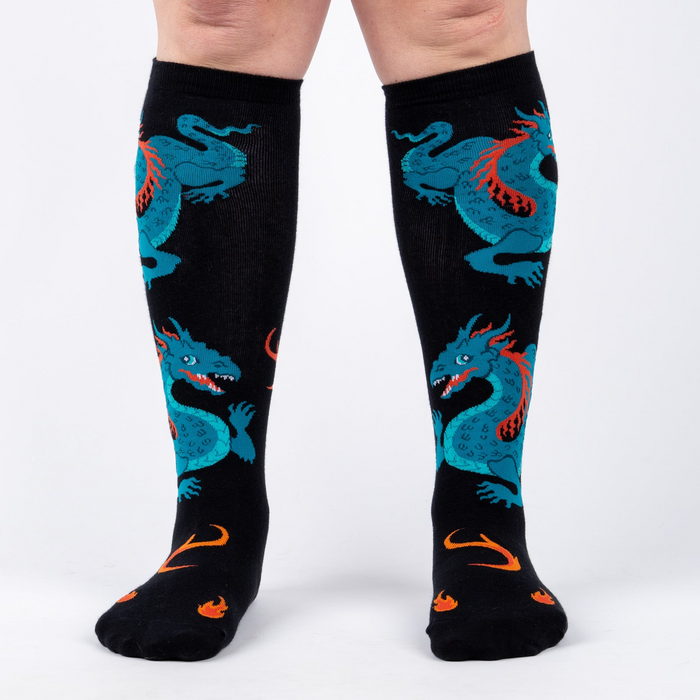 Front view of model wearing a pair of black knee-high socks with teal dragons and orange flames.