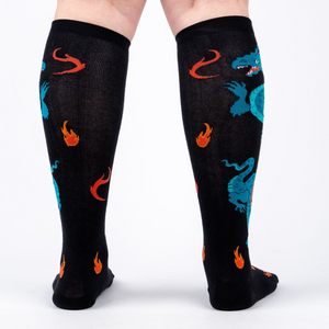 Back view of model wearing a pair of black knee-high socks with teal dragons and orange flames.