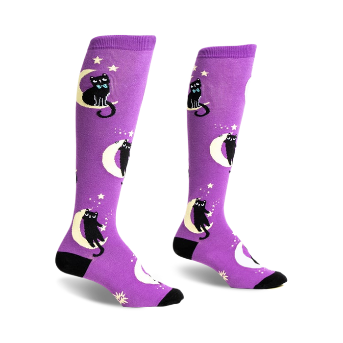 Pair of purple knee-high socks with black cats wearing bow ties sitting on crescent moons and stars.