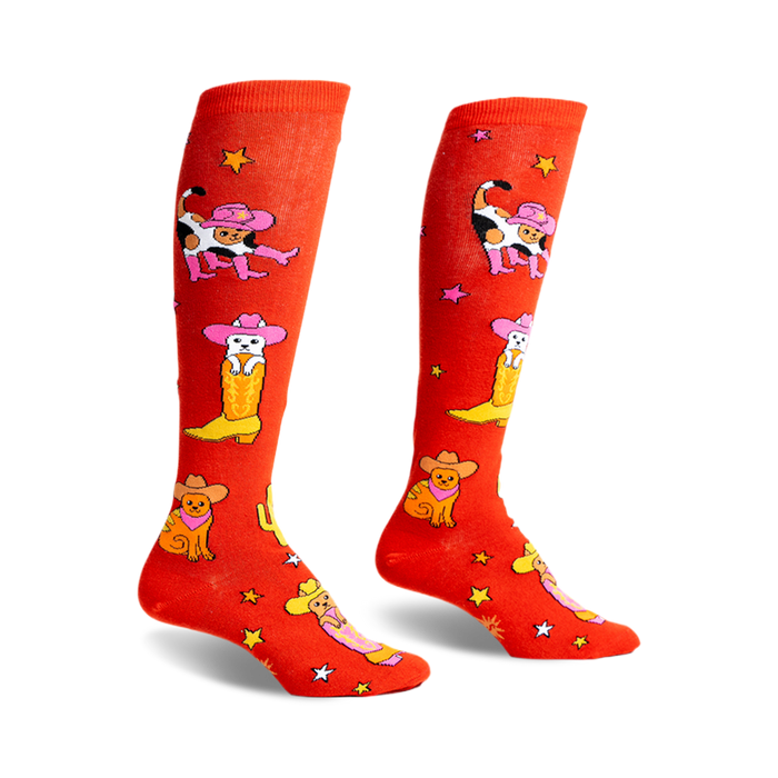 Pair of orange knee-high socks with a fun design of cats wearing cowboy hats and boots.  Stars and cacti are also featured.