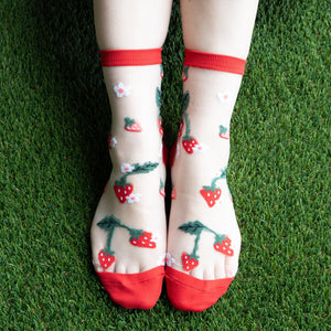 Lifestyle shot of the strawberry socks on a person's feet, worn outdoors on artificial grass.