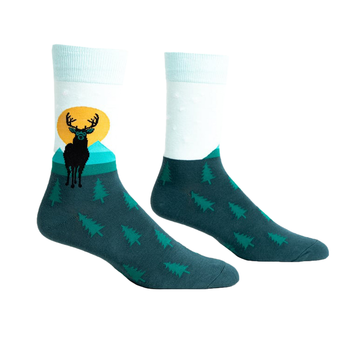 Pair of teal and mint crew socks featuring a black deer silhouette against a yellow sun and teal mountains.  Small pine trees cover the bottom.