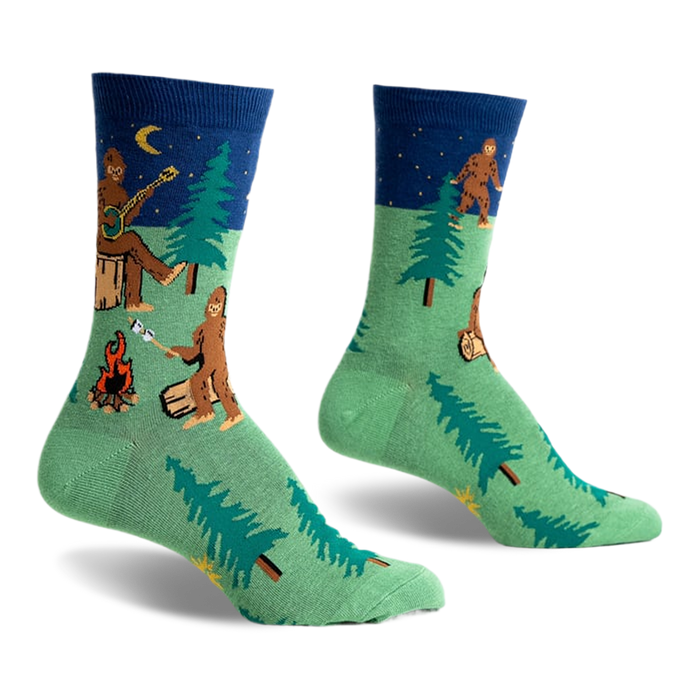 Crew socks in green and navy blue featuring a Bigfoot camping scene with trees, a campfire, and a Bigfoot playing a banjo under a starry night sky.