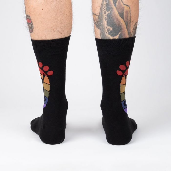 Rear view of the black 'Squatch and Learn' socks, highlighting the full rainbow footprint design on both socks.