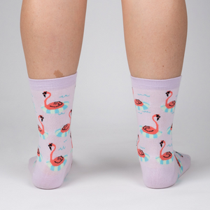 Back view of a person wearing lavender crew socks featuring a repeating pattern of flamingos on inflatable rings.