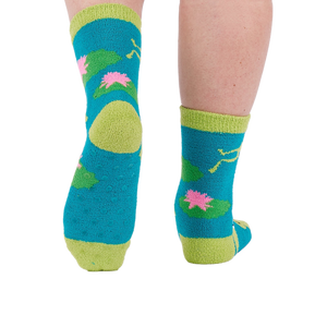 A person's legs and feet, viewed from behind, wearing the fuzzy teal blue slipper socks with visible grippers on the soles.
