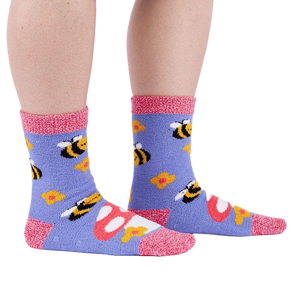 Person wearing fuzzy periwinkle slipper socks with bee, mushroom, and flower patterns, side view.