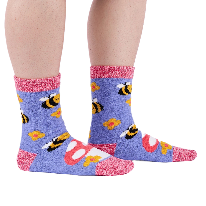 Person wearing fuzzy periwinkle slipper socks with bee, mushroom, and flower patterns, side view.