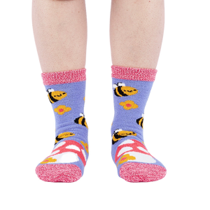 Person wearing fuzzy periwinkle slipper socks with bee, mushroom, and flower patterns, front view.