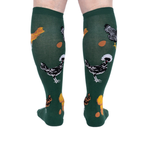 Person wearing dark green knee-high socks patterned with various chickens and eggs, standing, back view.