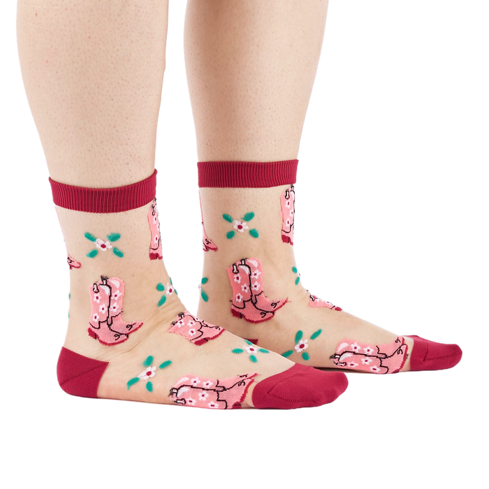 A person's legs and feet, wearing sheer pink cowboy boot socks from the side. Legs are bare against a white background.
