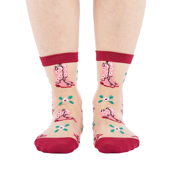 A person's legs and feet, wearing sheer pink cowboy boot socks, viewed from the front against a white background.