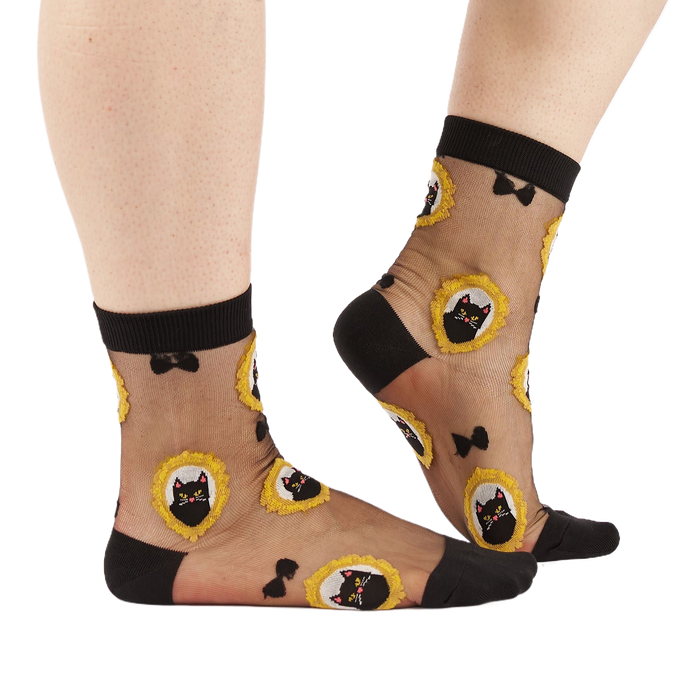 Person's lower legs and feet wearing the sheer black cat socks, standing on a white background.