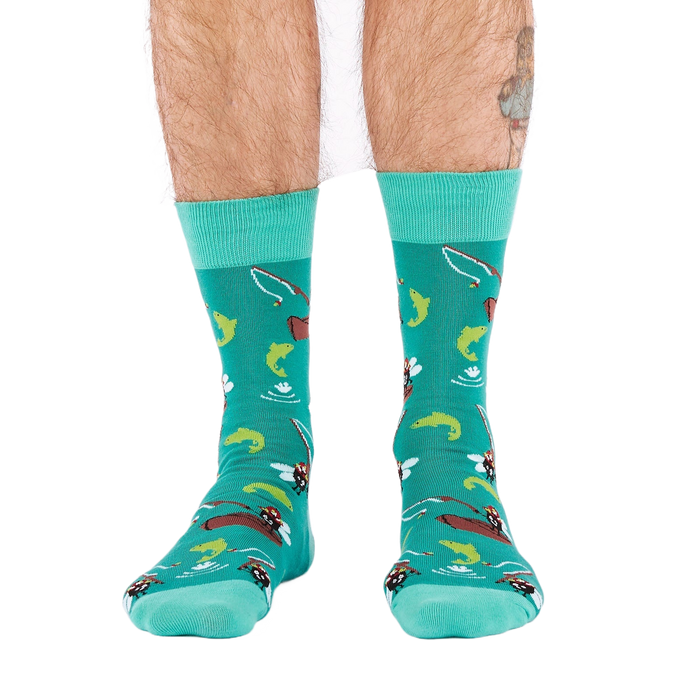 Front view of a person wearing teal fly fishing socks, showing leg hair and a partial tattoo on the right calf.