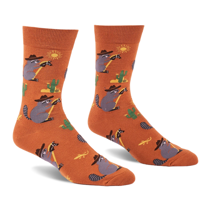 A pair of burnt orange crew socks with cartoon raccoons in cowboy hats lassoing, green cacti, yellow suns, and lizards.