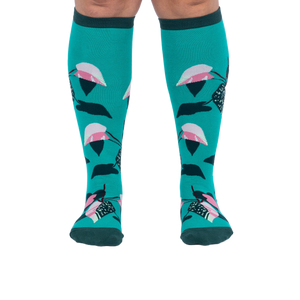Front view of a person's legs wearing teal knee-high socks with pink and dark green philodendron leaves.