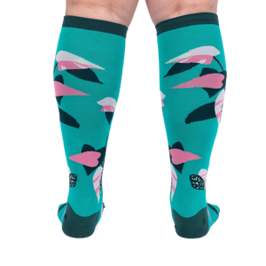 Back view of a person's legs wearing teal knee-high socks with pink and dark green philodendron leaves.
