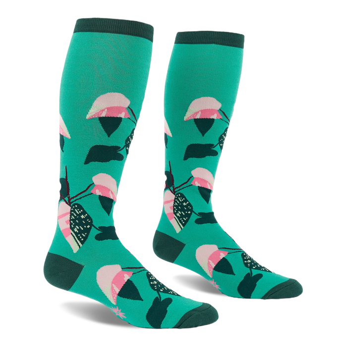 Pair of knee-high teal socks with a repeating philodendron leaf pattern in pink, white, dark green, and black. Dark green cuffs, heels, and toes.