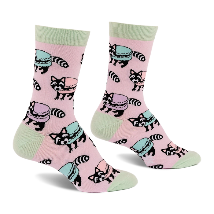 Pair of pink crew socks with light green accents, featuring a repeating pattern of cartoon raccoons and pastel macarons.