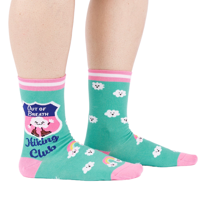 A person's legs wearing teal 'Hiking Club' crew socks, posed on a white background. Left sock shows shield design.