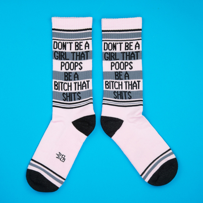 A pair of pink crew socks with black and grey stripes, featuring bold text, laid flat on a blue background.