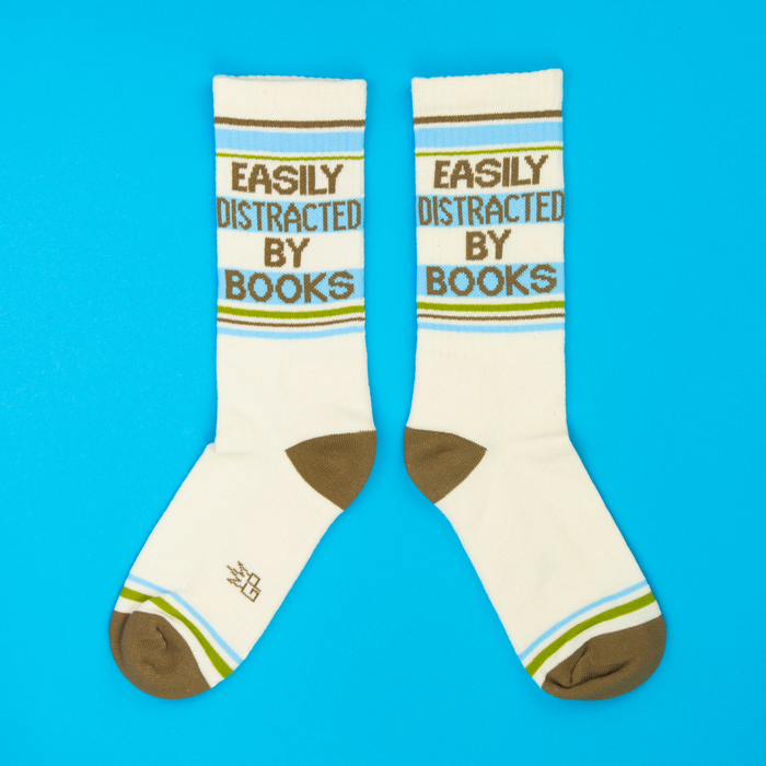 Two cream crew socks with book text, brown, blue, and green stripes laid flat on a bright blue surface.