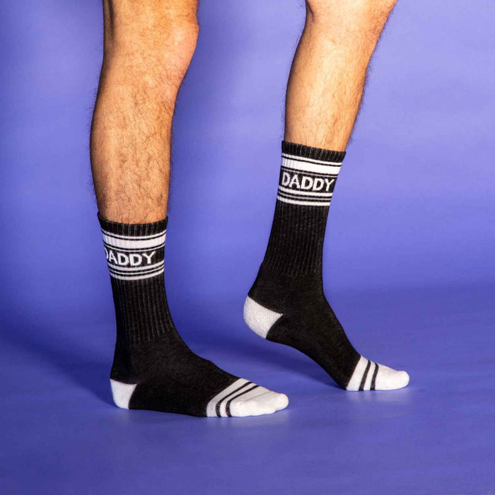 Lifestyle shot: Man's legs wearing 'Daddy' socks, against a purple background, this time standing.