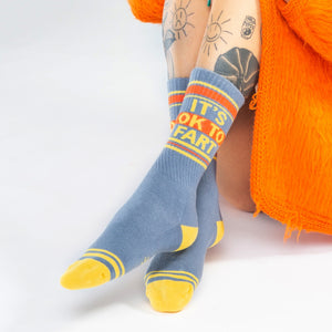 Close-up shot: 'It's Ok to Fart' socks on a person's legs; the focus is on the socks' design and texture.