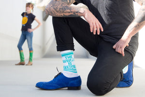 A man with tattoos on his arms is kneeling on the ground. He is wearing black pants, white socks that say 