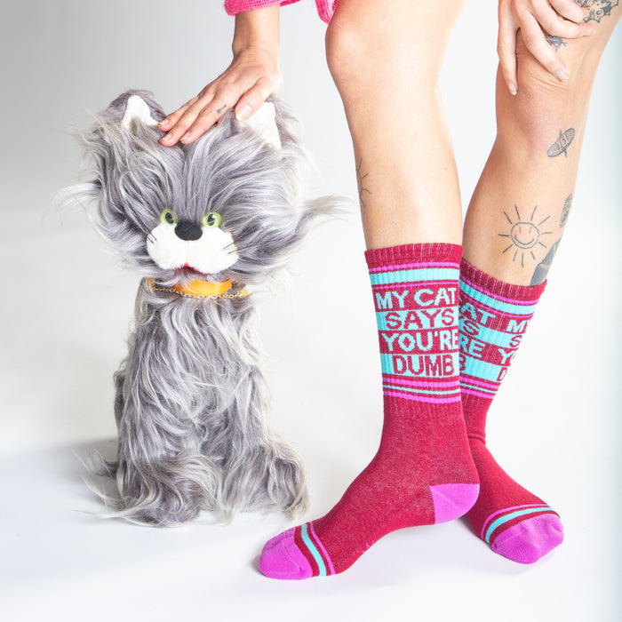 Lifestyle photo showing a model wearing the 'My Cat Says You're Dumb' socks with a fluffy gray cat toy.