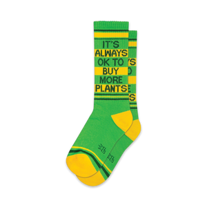 Pair of green and yellow crew socks with the text 'It's Always Ok To Buy More Plants' in black.  Features yellow and green stripes at the cuff.