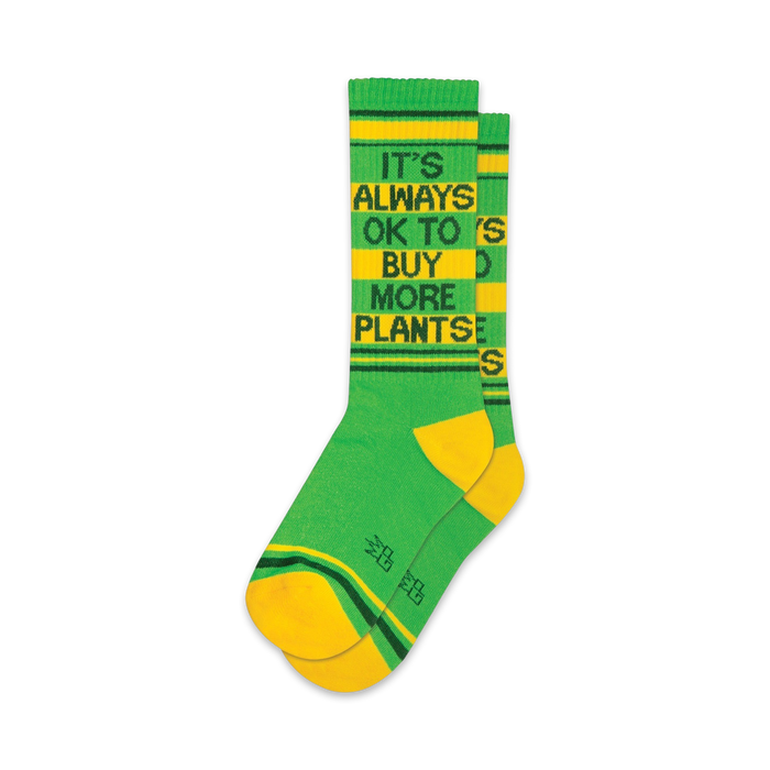 Pair of green and yellow crew socks with the text 'It's Always Ok To Buy More Plants' in black.  Features yellow and green stripes at the cuff.