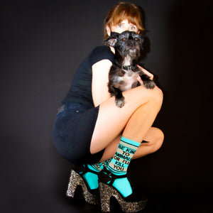 Lifestyle photo: Person wearing the 'Be Kind To Animals' socks and holding a small dog.  Black background.