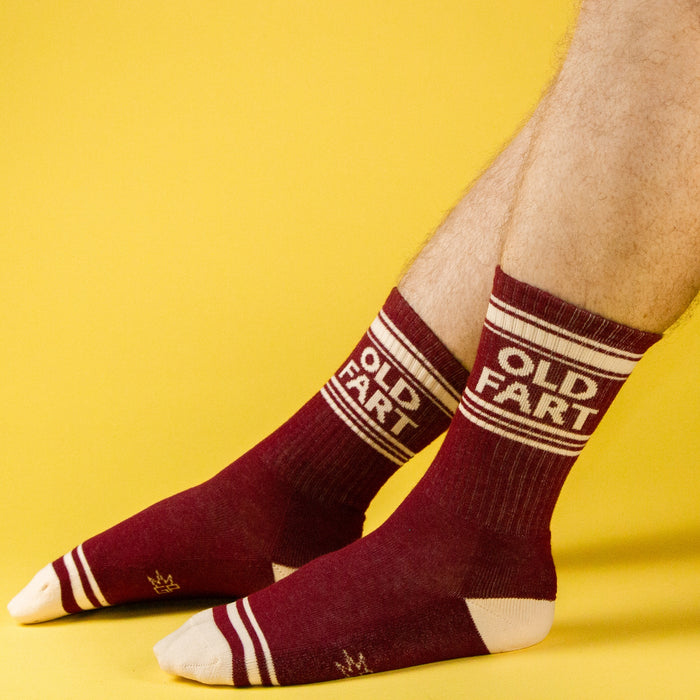 Lifestyle shot of hairy male legs wearing the 'Old Fart' socks against a yellow background.
