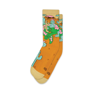 Pair of crew socks in mustard yellow with a whimsical design of a lizard lounging amidst cacti and desert flowers.  The socks have off-white cuffs.