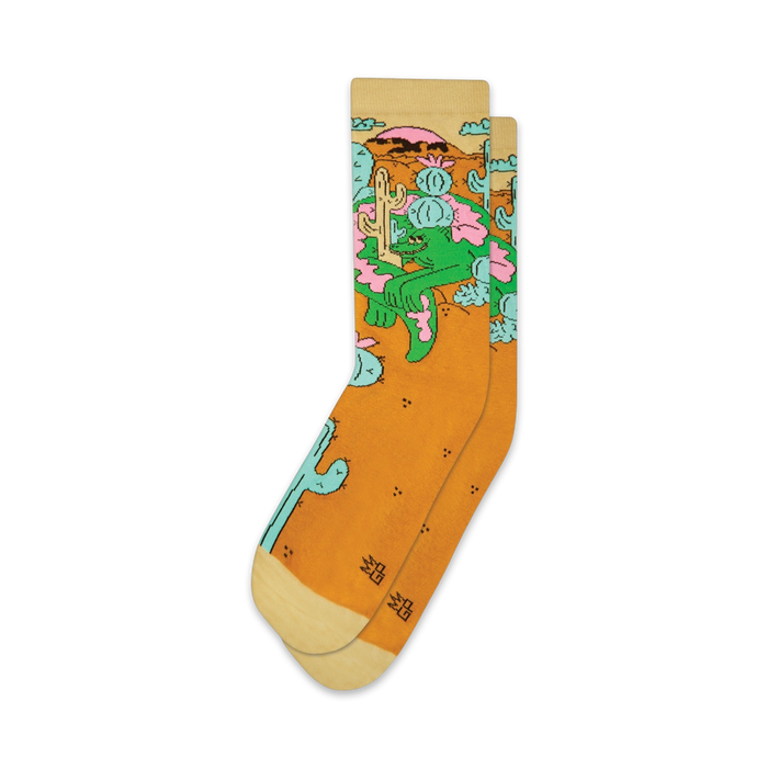 Pair of crew socks in mustard yellow with a whimsical design of a lizard lounging amidst cacti and desert flowers.  The socks have off-white cuffs.