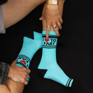 Lifestyle shot of a person's legs wearing the 'I ♥ To Fart' socks, sitting against a black background.