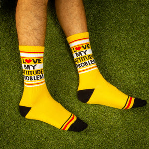 Lifestyle shot: Person wearing 'I Love My Attitude Problem' yellow crew socks on a green grass background.