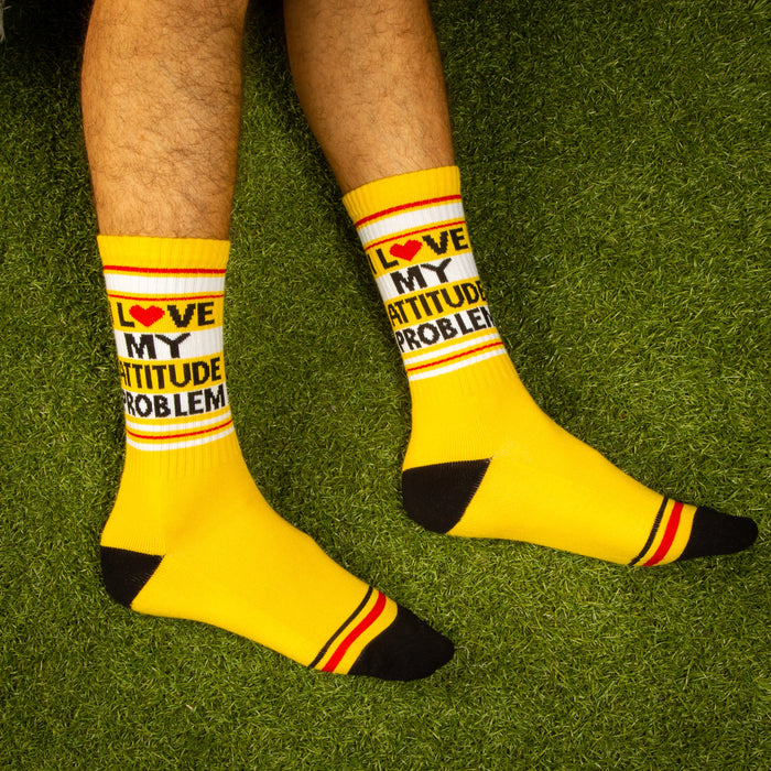 Lifestyle shot: Person wearing 'I Love My Attitude Problem' yellow crew socks on a green grass background.