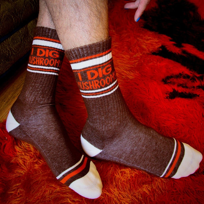 Lifestyle shot of 'I Dig Mushrooms' socks on a person's legs against a red fuzzy background.